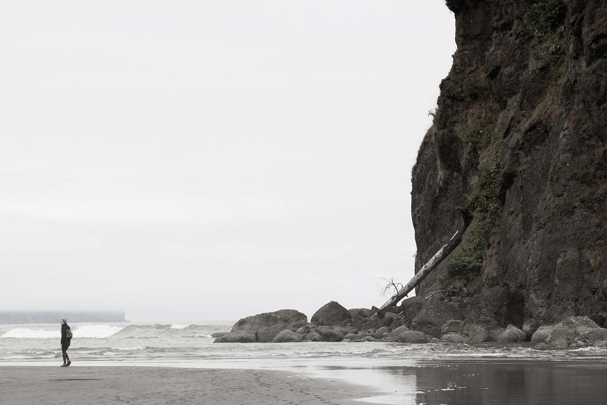 ruby beach person standing behind mountain in front of large body of water during daytime beach